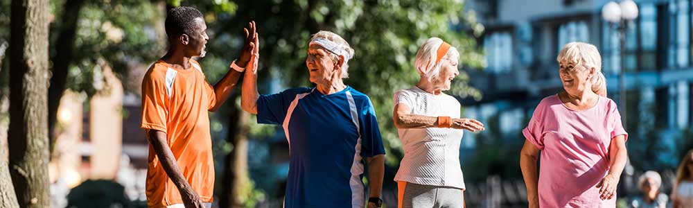 four seniors walking in a park and giving a high five